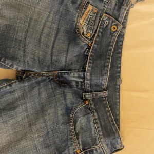 Lågmidjade diesel jeans - Lågmidjade utsvängda däck jeans med cool bältes detalj och revor  En av bältesöglorna har gått sönder  Storlek 26