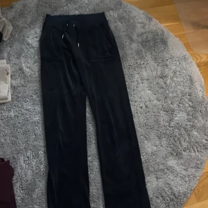 Svarta mjukisbyxor och tröja Juicy Couture XS och l - Svarta mjukisbyxor och tröja från Juicy Couture i storlek XS och LByxorna har bred resår i midjan med snörning, fickor med lock och silvriga knappar framtill. Materialet är mjukt och glansigt, typ sammet, och modellen är loose med raka ben.
