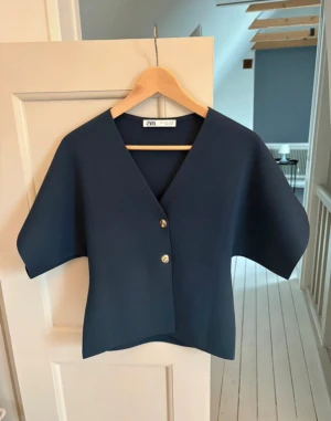 Mörkblå blus från Zara med knappar - Snygg mörkblå blus från Zara med v-ringning och två guldfärgade knappar framtill. 