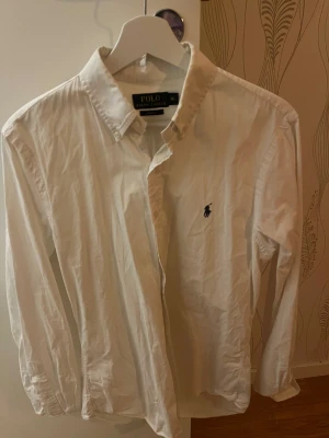 Vit skjorta Polo Ralph Lauren - Vit skjorta från Polo Ralph Lauren i slim fit med klassisk krage och knappar framtill. Broderad logga på bröstet. Långärmad och tillverkad i mjuk bomull.