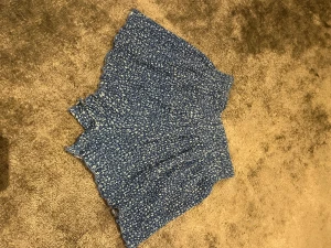 Blå blommig kortkjol från Zara - Supersöt blå kortkjol från Zara med små vita blommor över hela tyget. Kjolen har en smockad, stretchig midja och volangkant nedtill som ger en skön och flowy känsla. Perfekt för dig som gillar en feminin och chill stil.