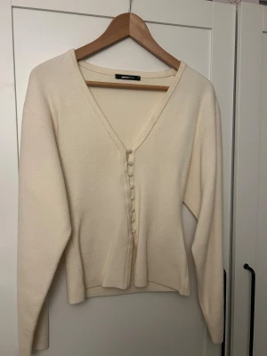Beige kofta med v-ringning Gina Tricot - Beige kofta från Gina Tricot i storlek XS. Koftan har v-ringad hals och dekorativa knappar framtill. Långärmad och tillverkad i mjukt stickat material.