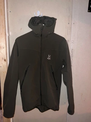 Mörkgrön vindjacka Haglöfs S - Säljer en mörkgrön Haglöfs Natrix Hood Men vindjacka i storlek S. Jackan har huva, två snedställda fickor med dragkedja och hel dragkedja framtill. Perfekt för utomhusaktiviteter och har en clean, sportig look.