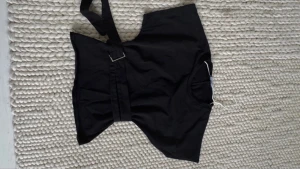 Svart bolerotopp med bälte - Cool svart bolerotopp med breda axlar och ett snyggt bälte med metallspänne framtill. Toppen är ärmlös och har en croppad passform