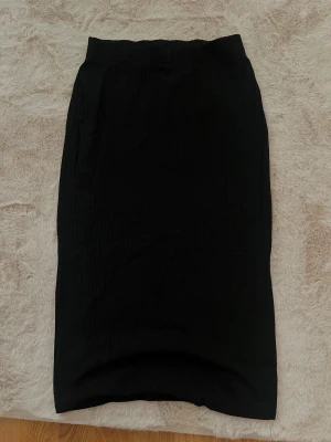 Svart ribbad kjol - En svart midikjol med ribbad struktur och elastisk midja med en slits nertill. Kjolen har en rak passform och är tillverkad i ett mjukt, stretchigt material som sitter bekvämt. Kjolen är från Only och är i storlek S. Superfin och helt oanvänd 