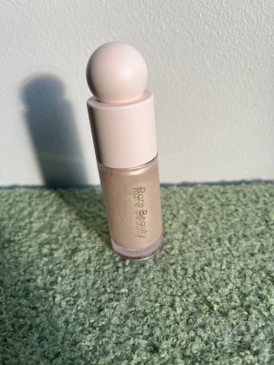 Rare Beauty Enlighten Liquid Highlighter - highlighter från Rare Beauty i nyansen Enlighten. Kommer i en stilren, ljusrosa flaska med rund kork och genomskinligt hölje som visar den skimrande, ljusa färgen. Perfekt för att ge glow till ansiktet. Aldrig använd
