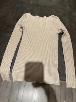 Beige ribbad långärmad tröja - Säljer en beige långärmad tröja med ribbad struktur och smal passform. Tröjan har en enkel design med rund hals och mjukt material som känns skönt mot huden. Perfekt att styla med jeans eller kjol för en clean look.💞💞