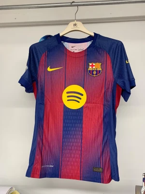 FC Barcelona Lamine Yamal #10 matchtröja - Säljer en officiell FC Barcelona matchtröja från Nike med Lamine Yamal och nummer 10 på ryggen. Tröjan är kortärmad, har klassiska blå och röda ränder, gula detaljer och flera patchar, bland annat Champions League och UEFA Foundation. Materialet är lätt och andas, perfekt för fotboll.