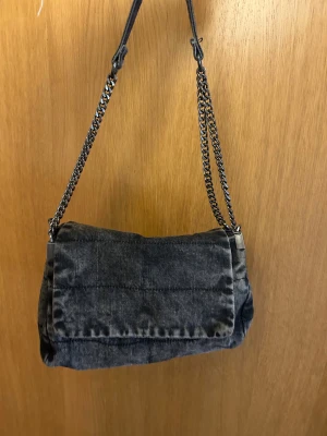 Mörkgrå Zara väska - Snygg mörkgrå axelväska med metallkedjor som axelrem. Väskan har flera fack och dragkedjor för förvaring. 