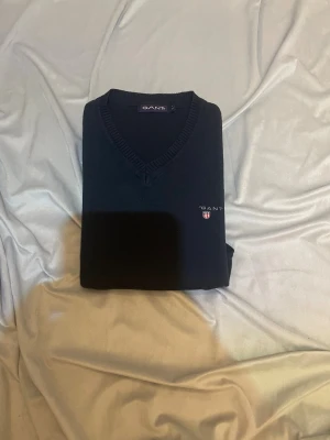 Marinblå stickad tröja från GANT passa xs eller 150-160! - Snygg marinblå stickad tröja från GANT i storlek S men passar xxs eller 150-160 både till men och kvinnor . Tröjan har v-ringad hals, ribbade muddar och GANT-logga med broderat emblem på bröstet. Perfekt för dig som gillar klassisk stil med en modern touch. Den passar till en tjej som har storlek  XS/S men för man typ XS/XXS/150-160! Passar bra nu för vintern.