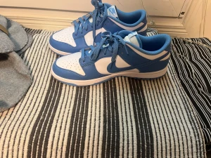 Nike Dunk Low blå och vita sneakers - Kom privat för prisförslag :Nike Dunk Low sneakers i fräscht blått och vitt. Klassisk låg modell med rund tå, snörning och platt sula. Ovandel i skinn med perforerad tåbox för extra ventilation. Snyggt kontrasterande Nike-logga på sidan och hälen. Perfekt för dig som gillar streetwear och sportig stil.