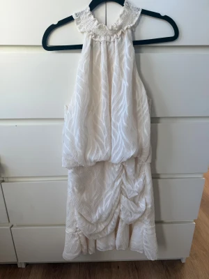 Vit kortklänning med volang från SHEIN - Supersöt vit kortklänning från SHEIN med volangdetaljer och smockad halsringning. Klänningen har ett subtilt mönster, pärlknappar i nacken och är ärmlös. Skulle säga att den är något liten i storlek då jag vanligtvis bär storlek S🤍