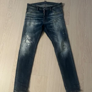 Blå Äkta jeans från Dsquared2 - Snygga blå jeans från Dsquared2 model     (cool Guy)med slitna detaljer och patch på bakfickan.Jeansen har coola slitningar och tvättade partier som ger en trendig look. Jeansen är köpta på United fashion i Göteborg Storlek 48 motsvarar 31 i midja 