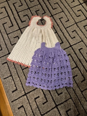 Två virkade sommarklänningar - Säljer två handvirkade klänningar i mjukt garn. En är vit med ljusrosa kantdetaljer och rund hals, den andra är lila med breda axelband och vackert hålmönster. Båda har söt volangkant nedtill och är perfekta för varma dagar. Den vita är 2-3 år och den lila är 1-2 år. 250 kr st