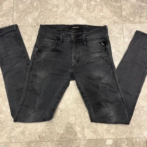 Replay anbass - Snygga svarta jeans från Replay med diskreta slitningar och tvättad look. Modellen har fem fickor, smal passform och klassisk knappgylf. Materialet är stretchigt jeans och bakfickorna har Replay-logga. Perfekt för dig som gillar en modern och avslappnad stil.