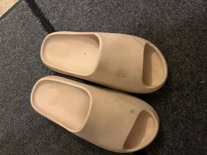 Beige slides med räfflad sula - Säljer ett par beige slides med öppen tå och chunky räfflad sula. De har en minimalistisk design och är gjorda i syntetmaterial, perfekta för chill dagar. Diskret logga på fotbädden. Sköna att glida runt i och passar dig som gillar enkel stil.