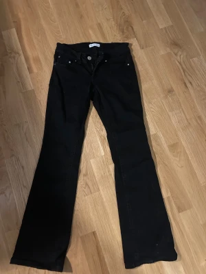 Svarta bootcut jeans från Perfect Jeans - Svarta jeans från Perfect Jeans i storlek 36 med klassisk femficksdesign och snygga silverknappar på bakfickorna. Modellen har bootcut-ben och dragkedja fram. Perfekt för dig som gillar en tidlös look med lite extra edge.