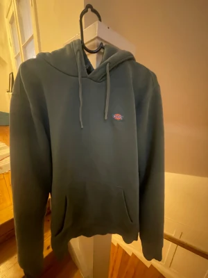 Mörkgrön hoodie från Dickies M - Säljer en mörkgrön hoodie från Dickies i storlek medium. Tröjan har huva med snörning, Dickies-logga på bröstet och en stor magficka. Materialet är mjukt och känns som bomull, perfekt för chill dagar. Långärmad och loose fit.