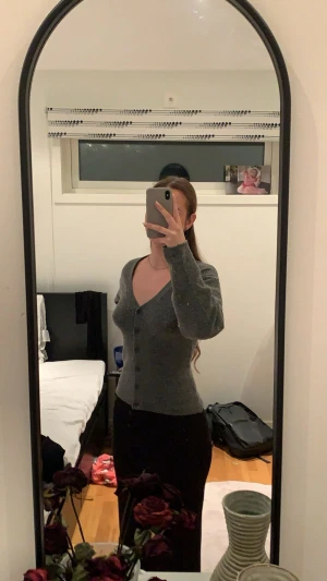 Grå kofta med knappar - Snygg grå kofta med v-ringning och knappar framtill. Modellen är figurnära med långa ärmar och mjukt stickat material som känns skönt mot huden. Perfekt att slänga på sig när det är lite kyligare ute.