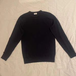 Mörkblå merinoulltröja John Henric - Snygg mörkblå stickad tröja från John Henric i storlek S, tillverkad i 100% merinoull. Klassisk rund hals och långärmad modell med ribbade muddar vid ärmslut och nederkant. Perfekt för dig som gillar stilrena och bekväma plagg.