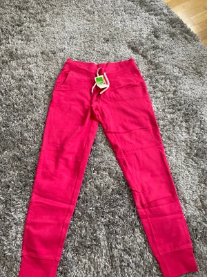 Rosa mjukisbyxor Race Marine strl 36 - Snygga rosa mjukisbyxor från Race Marine Essentials med vit snörning i midjan och ribbade muddar vid bensluten. Tillverkade i ekologisk bomull, perfekt för chill eller träning. Klassisk passform och bekväma fickor framtill.