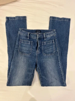 Blå bootcut jeans från J.Crew, stl 25 - Snygga blå jeans från J.Crew i bootcut-modell. Jeansen har två stora framfickor och två bakfickor, klassisk jeansknapp och bälteshällor. Materialet är slitstarkt denim i bomull. Perfekt för dig som gillar retrovibbar och bekväm passform.