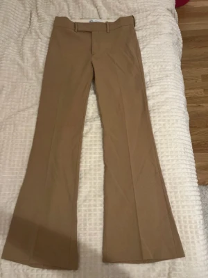 Beiga kostymbyxor från Zara - Kostymbyxor från Zara med utsvängda ben och pressveck. Byxorna har hällor för skärp och klassisk midja. 