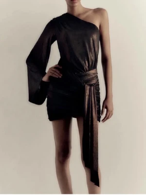 Svart glittrig one shoulder klänning zara - Säljer en svart glittrig kortklänning med one shoulder-design och lång ärm på ena sidan. Klänningen har en markerad midja med knytband och en snygg drapering som ger extra edge. Toppen skick!! Säljs ej längre ❤️❤️