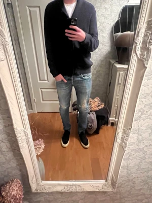 Blå slitna jeans från DonDup - Säljer ett par blå jeans från DonDup med slitningar på båda benen och lätt tvättad look. Jeansen har klassisk femficksmodell, normal midja och raka ben. Perfekta för en avslappnad och trendig stil.