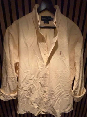 Gul skjorta från Ralph Lauren - Snygg gul skjorta från Ralph Lauren i klassisk modell med knappar hela vägen och broderad logga på bröstet. Skjortan är i 100% bomull och har lång ärm och normal passform. Perfekt för dig som vill ha en clean och stilren look. Skriv vid minsta fundering 💭 