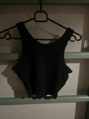 Svart ribbad croppad linnetopp - Säljer en svart croppad linnetopp med breda axelband och ribbad struktur. Toppen är ärmlös och har en enkel, stilren design som passar perfekt till jeans eller kjol. Perfekt för dig som gillar en clean och trendig look.