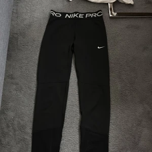 Svarta Nike Pro leggings - Säljer ett par svarta Nike Pro leggings med bred resår med Nike Pro-logga. De har en tight passform och en liten vit Nike Swoosh på låret. Perfekta för träning eller chill dagar. Största storleken på barnavdelning motsvarar xs/s