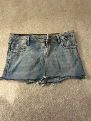 Ljusblå jeanskjol från LTB - Trendig ljusblå jeanskjol från LTB med rå kant nertill och klassiska fem fickor. Kjolen har en kort passform och slitna detaljer för en avslappnad look. Perfekt till sommaren och enkel att matcha med olika toppar.