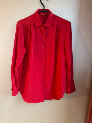 Härligt röd långärmad skjorta - En stilren röd skjorta med klassisk krage och knäppning framtill. Skjortan har långa ärmar med manschett och knappar, och är tillverkad i ett mjukt, lätt material med en förlåtande passform. Perfekt för dig som vill sticka ut med färg.