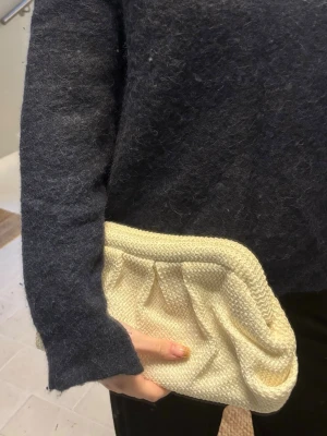 Vit kuvertväska - Trendig vit kuvertväska i randigt material med puffig form och fina veckdetaljer framtill. Perfekt accessoar för att lyfta din outfit med en unik touch. Lätt att bära i handen och passar till många olika stilar.