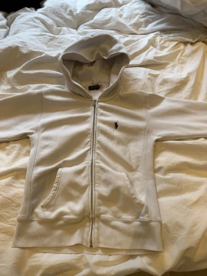 Vit hoodie från Polo Ralph Lauren - Klassisk vit hoodie från Polo Ralph Lauren med dragkedja framtill och broderad logga på bröstet. Hoodien har två fickor fram, ribbade muddar och en skön huva. Använd få gånger🤩