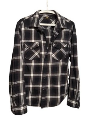 Svartvit rutig skjorta med fickor - Svart och vit rutig skjorta med klassisk krage och två bröstfickor med lock. Skjortan har långa ärmar och knäppning framtill. Perfekt för en avslappnad och cool stil.