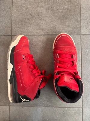 Jordan flight - Snygga röda Air Jordan sneakers med svarta och vita detaljer. Skorna har klassisk hög siluett, röda skosnören och ikonisk Jumpman-logga på sidan och sulan. Ovandelen är i mocka och textil, med vadderad plös och krage för extra komfort.