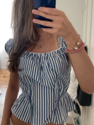 Blåvit randig blus med volang - Säljer en söt blåvit randig blus med volangdetaljer och spets vid halsringningen. Blusen har korta puffärmar och en smickrande passform som ger en romantisk vibe. Perfekt för dig som gillar en trendig och feminin stil.