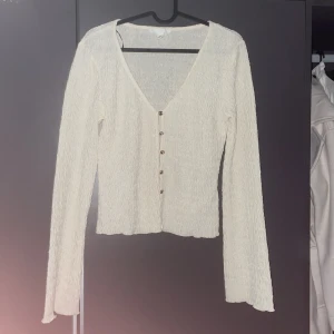 Krämvit blus med v-ringning från H&M - Krämvit blus från H&M med lång ärm, v-ringning och snygga knappar framtill. Materialet är lätt strukturerat och ger en cool vågig effekt. Perfekt för dig som gillar en enkel men ändå unik look. Använd 1 gång den är helt ny 
