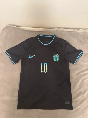 Neymar Jr svart brazil fotbollströja - Snygg svart fotbollströja från Nike med Brasilien-emblem och nummer 10 på bröstet. Tröjan har turkosa detaljer vid krage, ärmslut och Nike-logga. Tillverkad i lätt och ventilerande material, perfekt för träning eller match. PRIS KAN DISKUTERAS