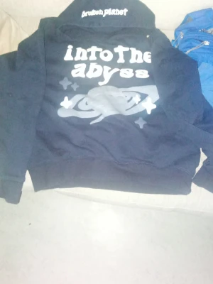 Svart hoodie Broken Planet Into the Abyss - Cool svart hoodie från Broken Planet med trycket 'into the abyss' och ett rymdmotiv på bröstet. Huva med broderad text och klassisk känguruficka. Perfekt för dig som gillar streetwear och unika prints.  OBS!!! PRIS KAN DISKUTERAS 