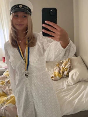 Student klänning  - Säljer en vit kort klänning med v-ringning och långa ärmar. Klänningen har fina broderade detaljer och knappar framtill. Perfekt för student eller sommarens tillfällen. Från bubbelroom. 38 men är som 36 