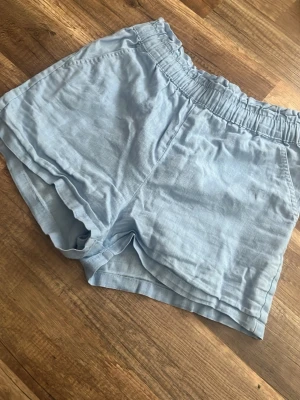 Ljusblå shorts med snörning - Säljer ett par ljusblå shorts med elastisk midja och snörning. De är tillverkade i ett mjukt och svalt material, perfekta för varma dagar. Shortsen har en avslappnad passform och är riktigt sköna att bära.
