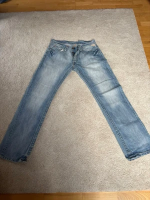 Ljusblå Replay jeans med raka ben - Snygga ljusblå jeans från Replay med klassisk femficksdesign och raka ben. Jeansen har slitna detaljer framtill och en läderpatch med Replay-logga bak i midjan. Perfekta för en avslappnad och trendig stil.