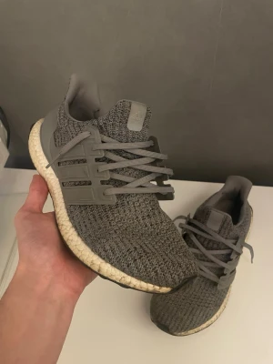 Grå Adidas Ultraboost sneakers - Säljer ett par grå Adidas Ultraboost sneakers med stickad ovandel och Boost-sula. Skorna har en modern design med plastdetaljer på sidorna och matchande grå skosnören. Perfekta för dig som gillar stilrena och bekväma sneakers. Dem är lite smutsiga men det går lätt att tvätta bort och det är inga skador eller problem med dem! 