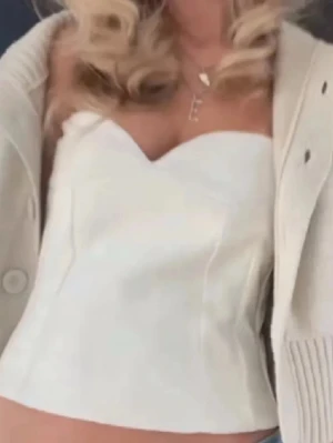 Vit axelbandslös korsettopp - Trendig vit korsettopp med axelbandslös design och snygg struktur. Toppen har en croppad passform och markerad byst, perfekt för att styla med jeans eller kjol. Enkel men stilren look som passar till många outfits.