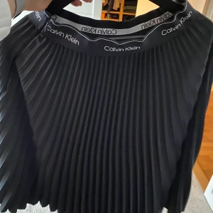 Pliserad kjol från Calvin Klein - Storlek 34, pliserad svart kjol med dragkedja i sidan. Använd 2 gånger. Ordinarie pris 1500kr
