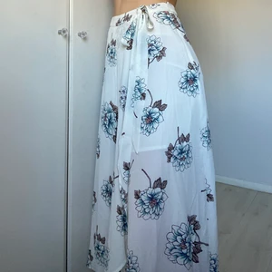 Somrig omlottkjol - Vit somrig, omlottkjol (knyts ej, dragkedja på sidan). Sitter något löst i midjan på mig (har ca 70cm i midjemått). Längre baktill. 100% polyester. Oanvänd!