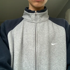 Grå/blå nike zipuptröja  - Sjukt snygg grå nike ziptröja med mörkblåa ärmar! Ungefär 1,5 år gammal och säljer pga att jag inte använder den längre. Sitter oversized på mig som är 191 cm men den ser inte för stor ut på folk som är kortare.